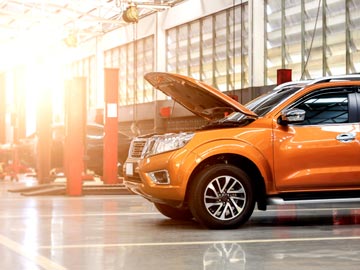 Ein orangefarbenes SUV steht in einer gut beleuchteten Auto-Werkstatt bei Autoankauf Elmshorn, dessen Motorhaube offen ist und den Motor zeigt.